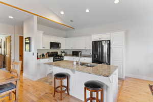 Kitchen with a kitchen island with sink, sink, black appliances, white cabinetry, and light stone counters