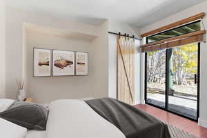 Bedroom with wood-type flooring, a barn door, and access to exterior