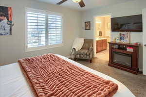 Bedroom with ensuite bathroom, light colored carpet, and ceiling fan