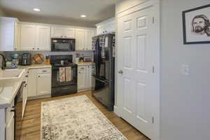 Kitchen featuring sink, black appliances, white cabinets, and light laminate wood-style floors