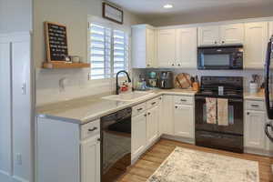 Kitchen with sink, black appliances, white cabinetry, and light  laminate wood-style flooring