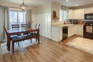 Kitchen featuring black appliances, sink, hanging light fixtures, white cabinetry, and light laminate wood-style floors