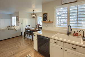 Kitchen featuring white cabinetry, a healthy amount of sunlight, black dishwasher, and hanging light fixtures