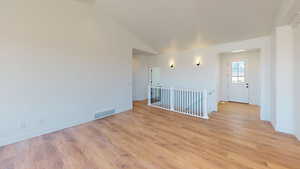 Empty room featuring light wood-type flooring and vaulted ceiling