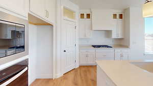 Kitchen featuring custom range hood, pendant lighting, black gas cooktop, light hardwood / wood-style floors, and white cabinetry