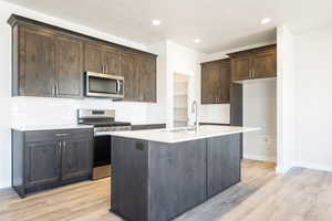 Kitchen with backsplash, stainless steel appliances, light hardwood / wood-style flooring, and a kitchen island with sink