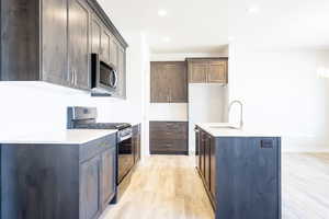 Kitchen featuring an island with sink, dark brown cabinets, sink, appliances with stainless steel finishes, and light hardwood / wood-style floors