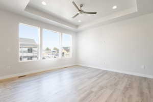 Spare room with light hardwood / wood-style floors, a raised ceiling, and ceiling fan