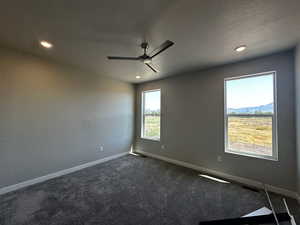 Unfurnished room with a mountain view, a textured ceiling, dark colored carpet, and ceiling fan