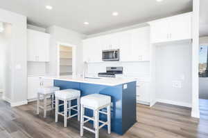 Kitchen featuring stainless steel appliances, light wood-type flooring, a center island with sink, and white cabinets