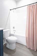 Full bathroom with toilet, shower / tub combo with curtain, hardwood / wood-style flooring, and vanity