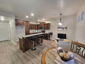 Kitchen with light hardwood / wood-style flooring, appliances with stainless steel finishes, decorative light fixtures, light stone counters, and dark brown cabinets