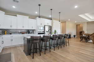 Kitchen featuring light wood-type flooring, an island with sink, hanging light fixtures, white cabinetry, and stainless steel appliances