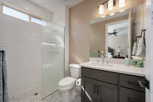 Bathroom featuring tile patterned floors, tiled shower, toilet, vanity, and ceiling fan