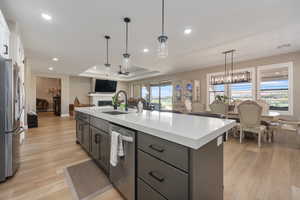 Kitchen with appliances with stainless steel finishes, a kitchen island with sink, light wood-type flooring, pendant lighting, and sink