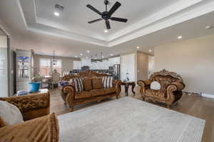 Living room with a tray ceiling, light hardwood / wood-style floors, and ceiling fan