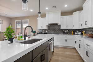 Kitchen with hanging light fixtures, white cabinetry, dishwasher, light hardwood / wood-style floors, and sink