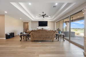 Living room featuring light hardwood / wood-style flooring, ceiling fan, and a raised ceiling