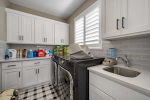 Clothes washing area featuring independent washer and dryer, cabinets, and sink