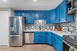 Kitchen with blue cabinetry, stainless steel appliances, backsplash, and light hardwood / wood-style floors