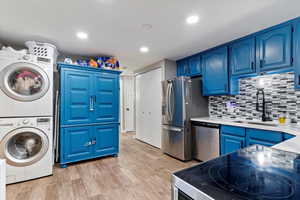 Kitchen featuring sink, blue cabinets, stainless steel appliances, light hardwood / wood-style flooring, and stacked washer and clothes dryer