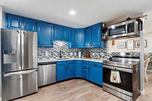 Kitchen featuring decorative backsplash, light hardwood / wood-style flooring, stainless steel appliances, sink, and blue cabinetry