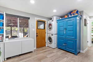 Clothes washing area with stacked washing maching and dryer, cabinets, and light wood-type flooring