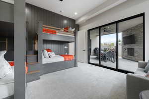 Carpeted bedroom with a stone fireplace, wood walls, and access to exterior