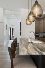 Kitchen featuring dark stone counters, sink, light wood-type flooring, and hanging light fixtures