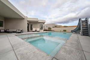 View of pool featuring an in ground hot tub, a patio, a water slide, and an outdoor hangout area