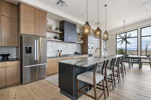 Kitchen with an island with sink, a kitchen breakfast bar, dark stone counters, light hardwood / wood-style floors, and stainless steel appliances