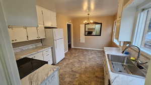 Kitchen featuring sink, white refrigerator, decorative light fixtures, a notable chandelier, and white cabinets