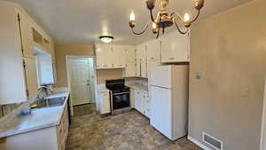 Kitchen with electric stove, sink, decorative light fixtures, white fridge, and a chandelier