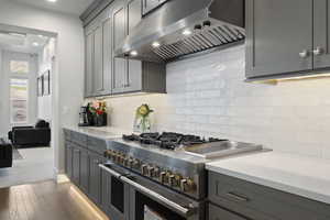 Kitchen with tasteful backsplash, range with two ovens, dark hardwood / wood-style flooring, gray cabinets, and ventilation hood