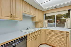 Kitchen featuring light tile patterned flooring, black dishwasher, sink, and light brown cabinetry