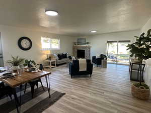 Living room with a stone fireplace, a textured ceiling, and light hardwood / wood-style flooring