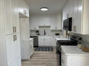 Kitchen featuring light hardwood / wood-style flooring, stainless steel appliances, sink, white cabinets, and light stone counters