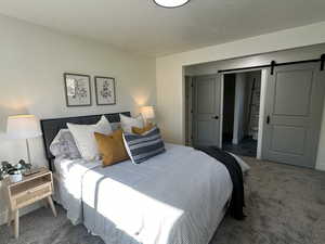 Bedroom featuring a textured ceiling, a barn door, and carpet flooring