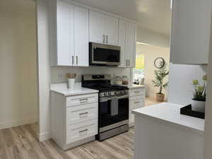 Kitchen featuring white cabinetry, stainless steel appliances, light stone countertops, and light hardwood / wood-style flooring