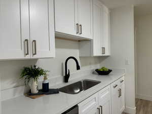 Kitchen with white cabinetry, light stone counters, sink, and light wood-type flooring