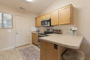 Kitchen with light brown cabinetry, light wood-type flooring, backsplash, NEW stainless steel appliances, and vaulted ceiling