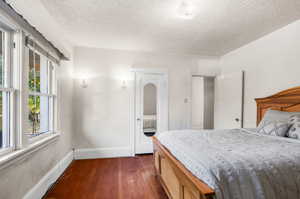 Bedroom with multiple windows, a textured ceiling, and dark hardwood / wood-style flooring