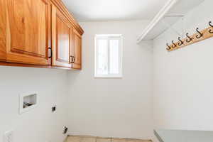 Washroom with washer hookup, light tile patterned floors, and cabinets