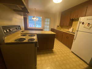 Kitchen featuring hanging light fixtures, extractor fan, electric stove, a notable chandelier, and white fridge