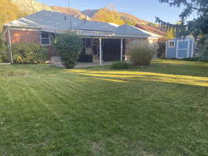 Back of house with a patio area, a mountain view, a storage shed, and a lawn