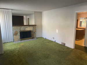 Unfurnished living room with a stone fireplace, a textured ceiling, and carpet floors