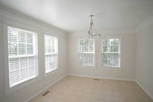 Spare room with a wealth of natural light, crown molding, and a chandelier