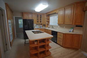 Kitchen with a breakfast bar area, sink, black appliances, a center island, and light wood-type flooring