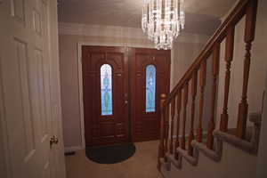 Foyer entrance featuring an inviting chandelier, crown molding, and tile patterned floors