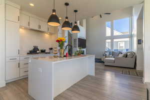 Kitchen featuring decorative backsplash, pendant lighting, a center island with sink, and light hardwood / wood-style floors